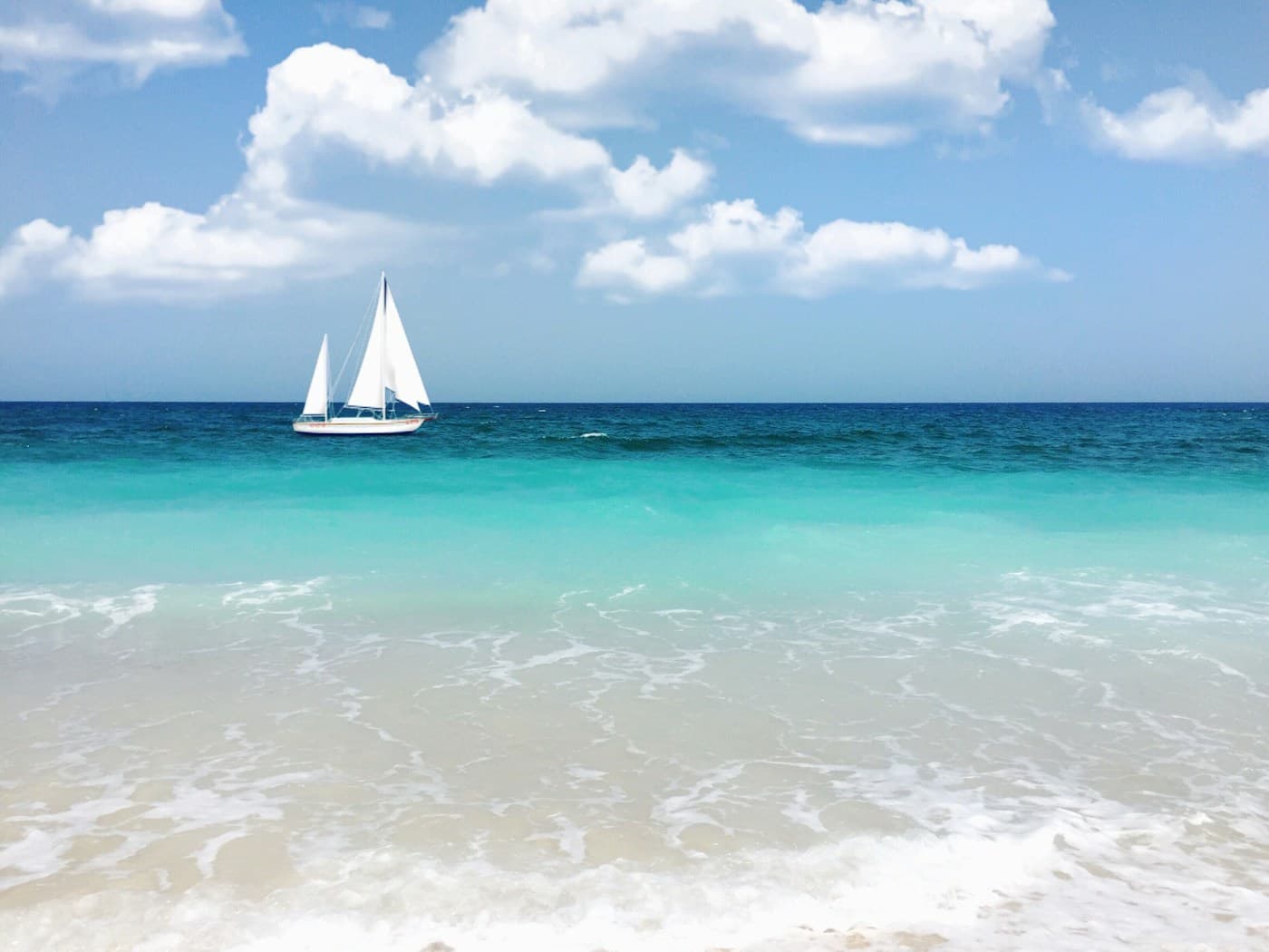 White sailing yacht passing a turquoise shoreline